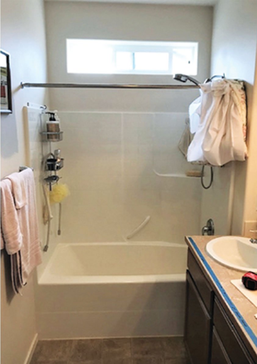 White tub and shower combo with wall surround, mounted shower rod, and compact vanity in a small bathroom remodel.