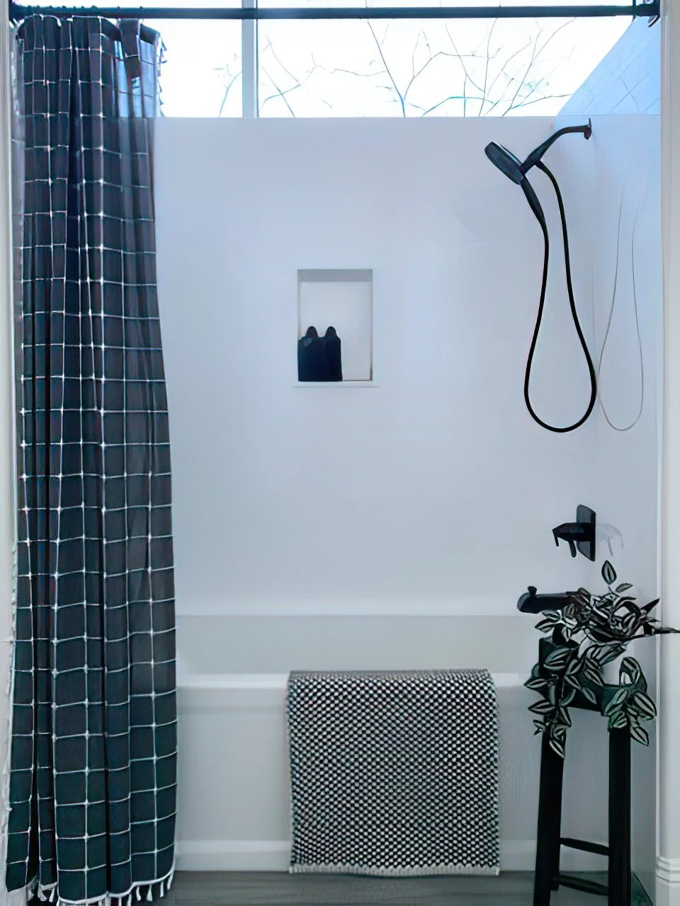 Modern tub and shower combination with white subway tile walls, black shower fixtures, and natural light window above.