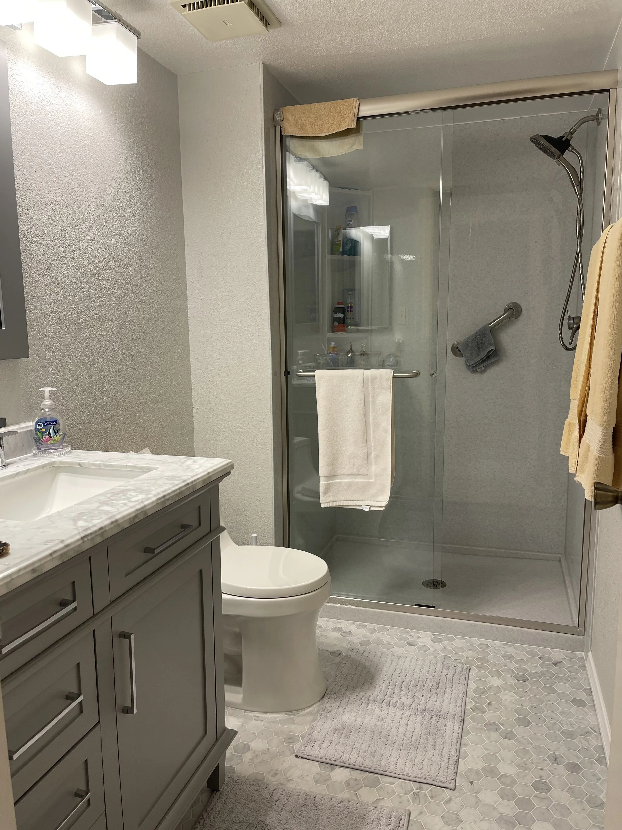 Walk-in shower remodel with gray stone surround, built-in corner bench seating, recessed shelving, and frameless glass panel enclosure