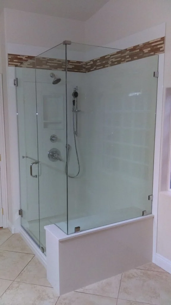 Frameless sliding glass shower enclosure with dark metal hardware, built-in product niche, and stone wall surround.