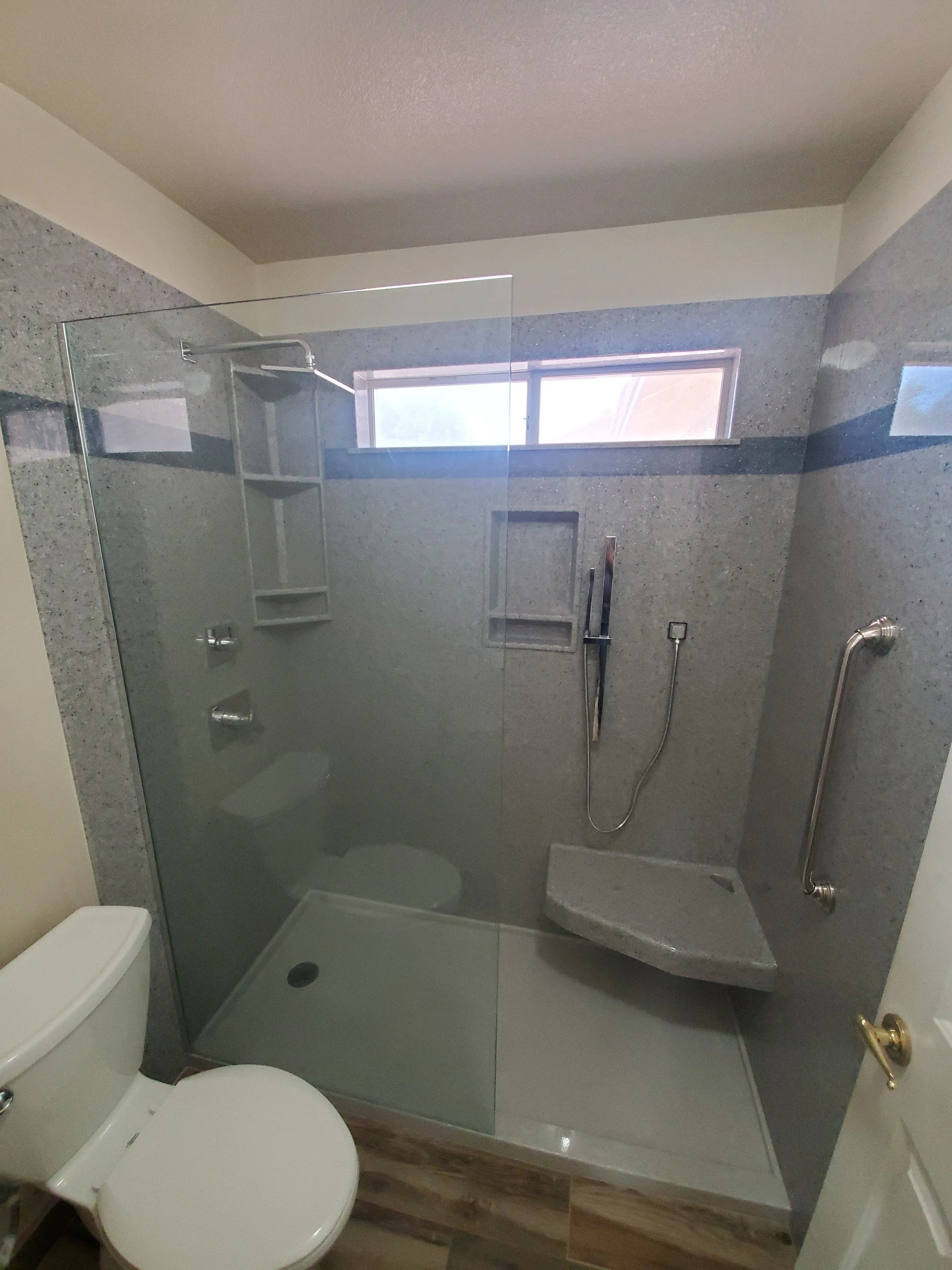 Accessible walk-in shower remodel with fold-down bench seating, grab bars, handheld shower head, and frameless glass panel in Southern Utah bathroom renovation