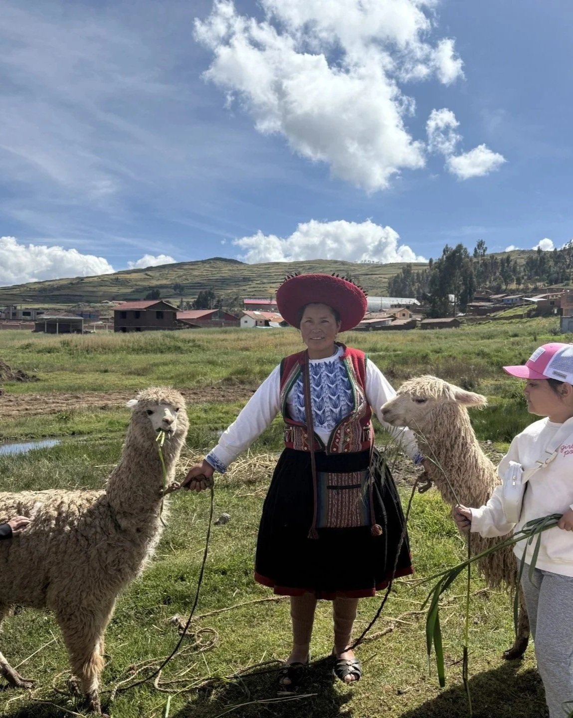 Peruvian woman in traditional dress holding two alpacas in a rural Andean village
