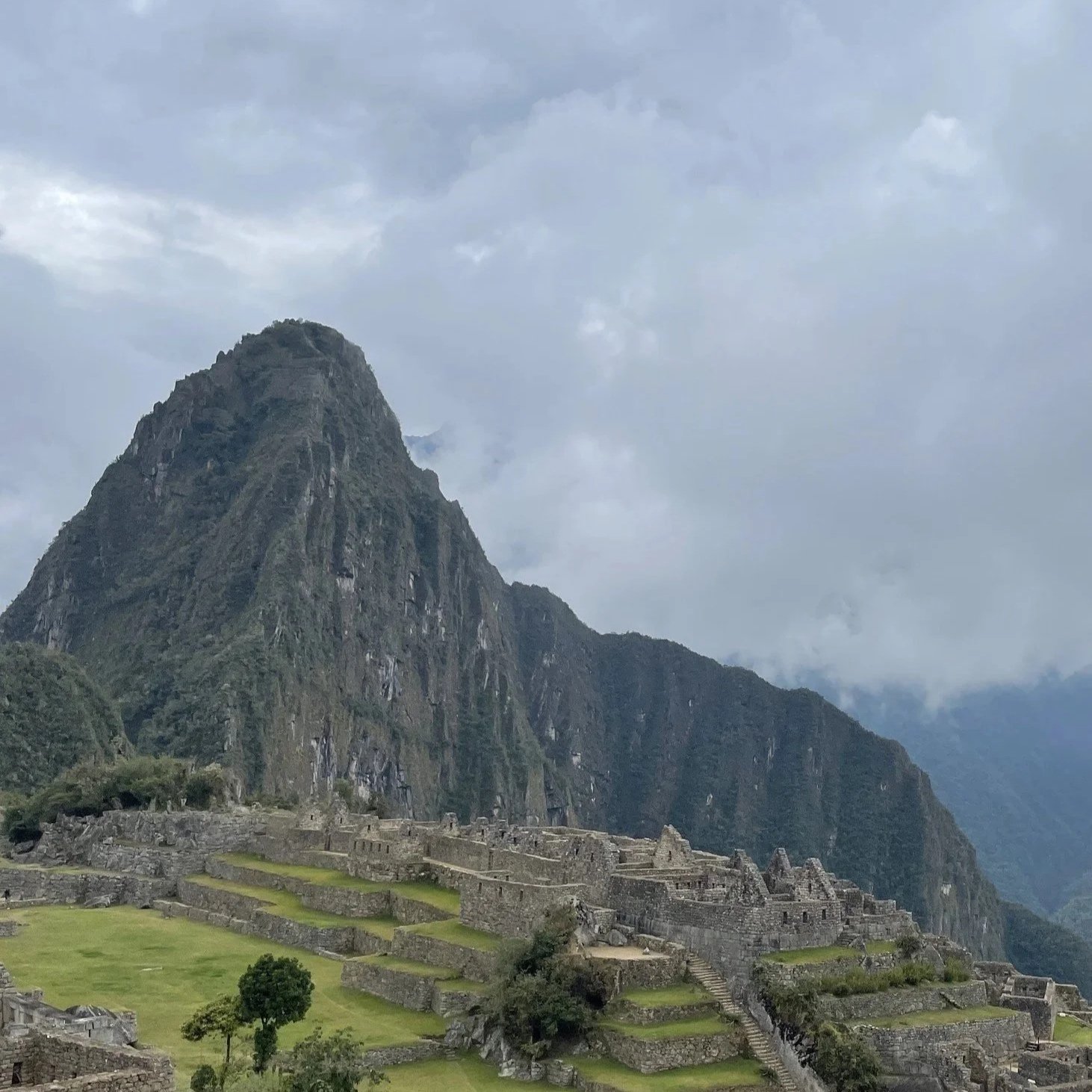 Machu Picchu ruins and terraces beneath Huayna Picchu mountain under a cloudy sky