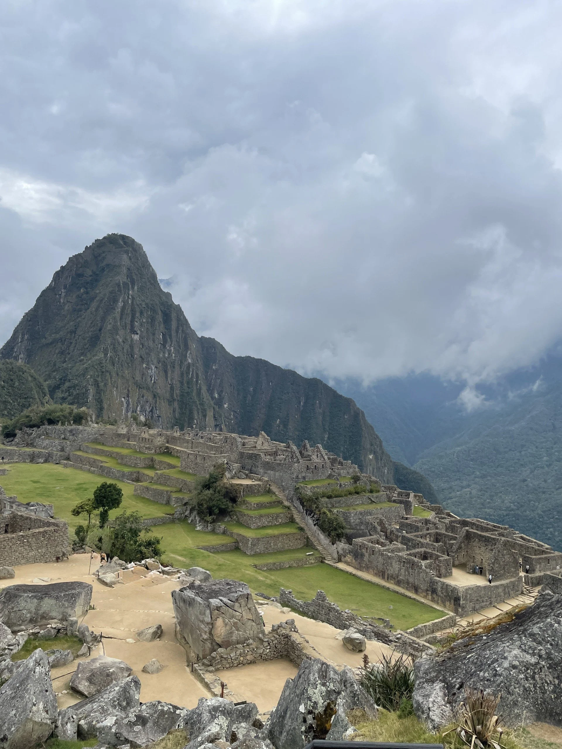 Machu Picchu ruins and terraces beneath Huayna Picchu mountain under a cloudy sky