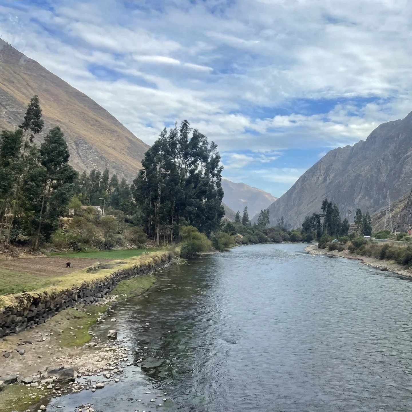 River flowing through Peru’s Sacred Valley, surrounded by mountains and trees under a cloudy sky