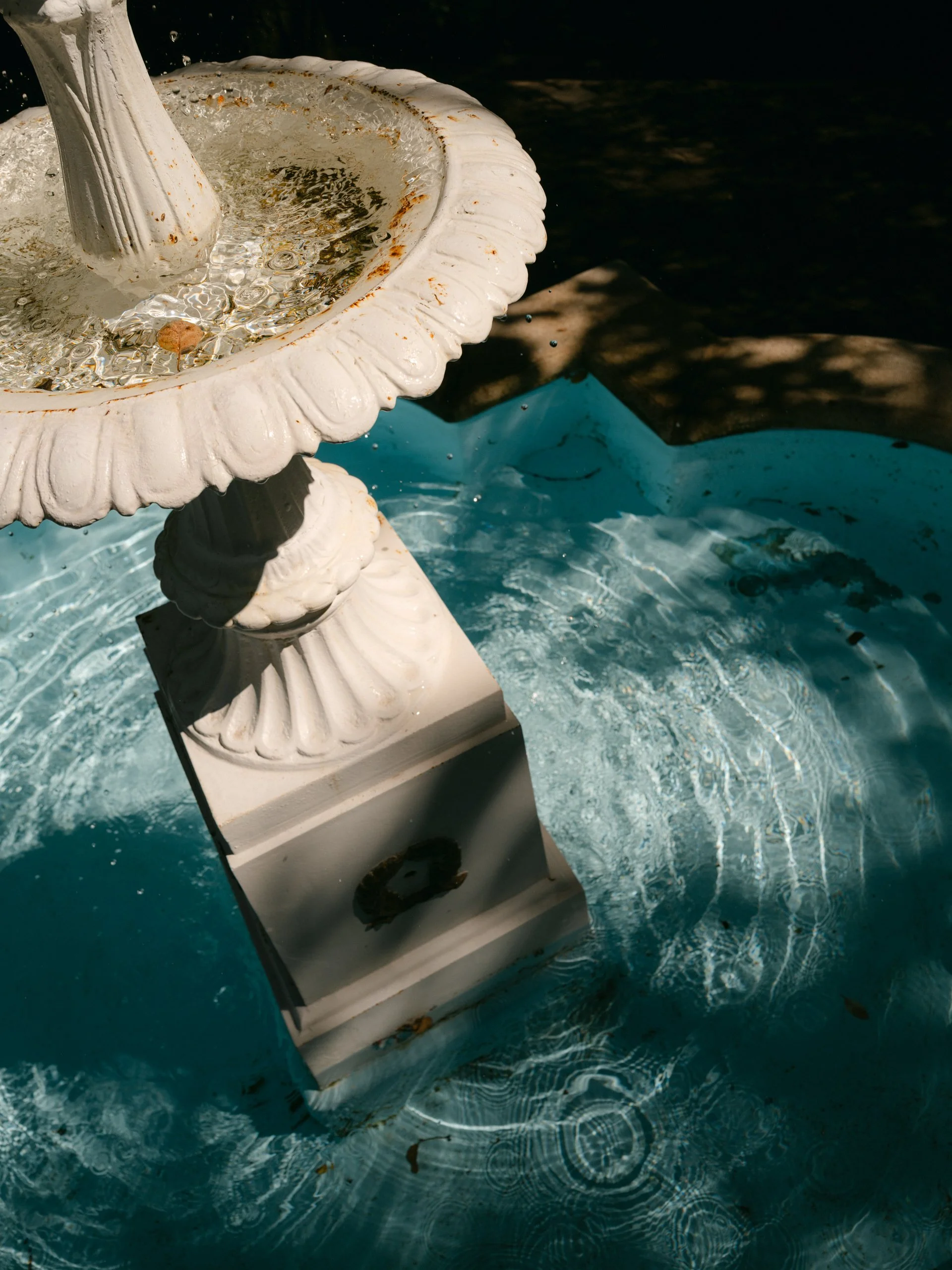 Close-up of a white ornamental fountain with water flowing into a small pool.