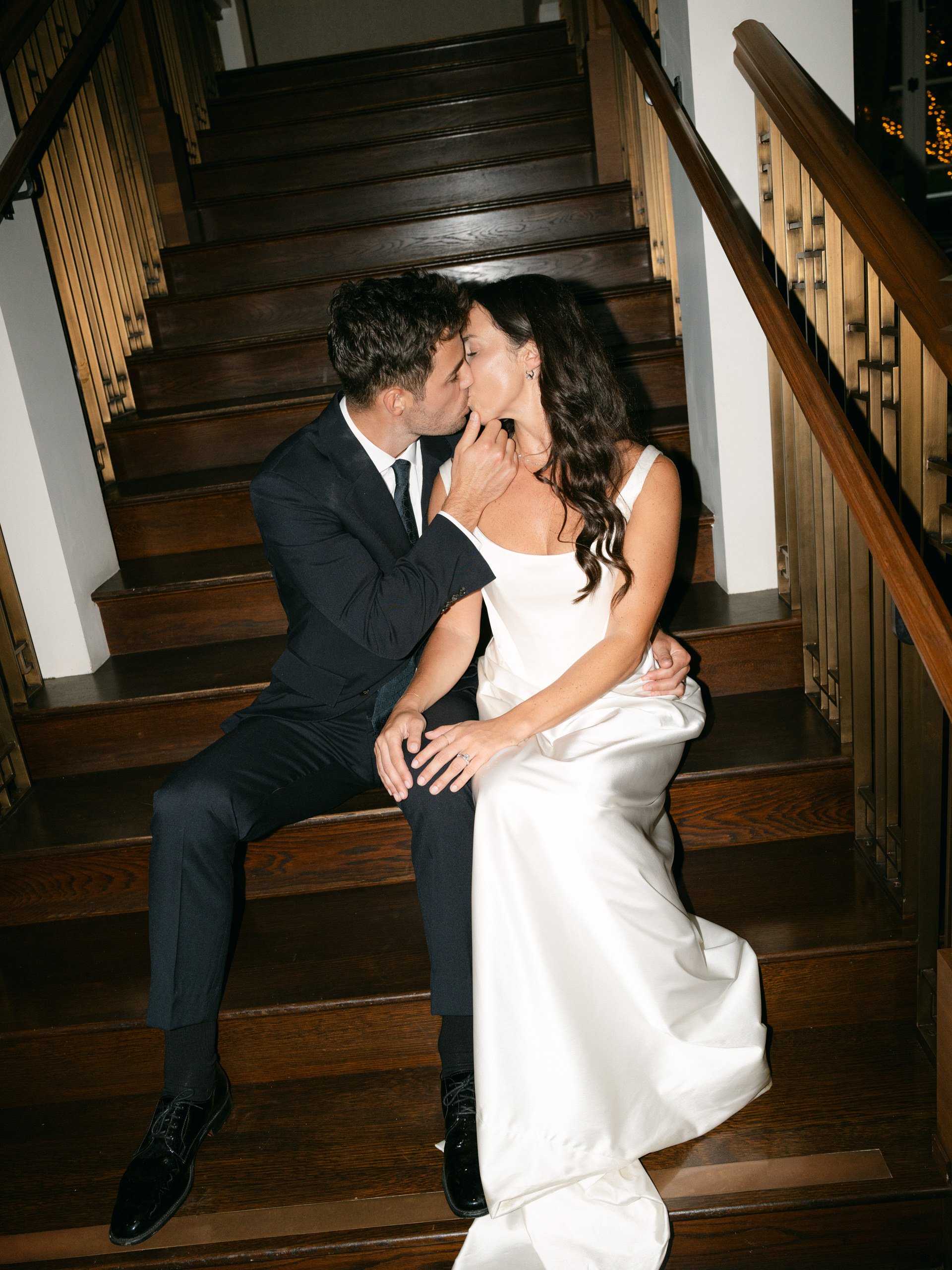 A couple dressed in formal wedding attire sharing a kiss on a wooden staircase.