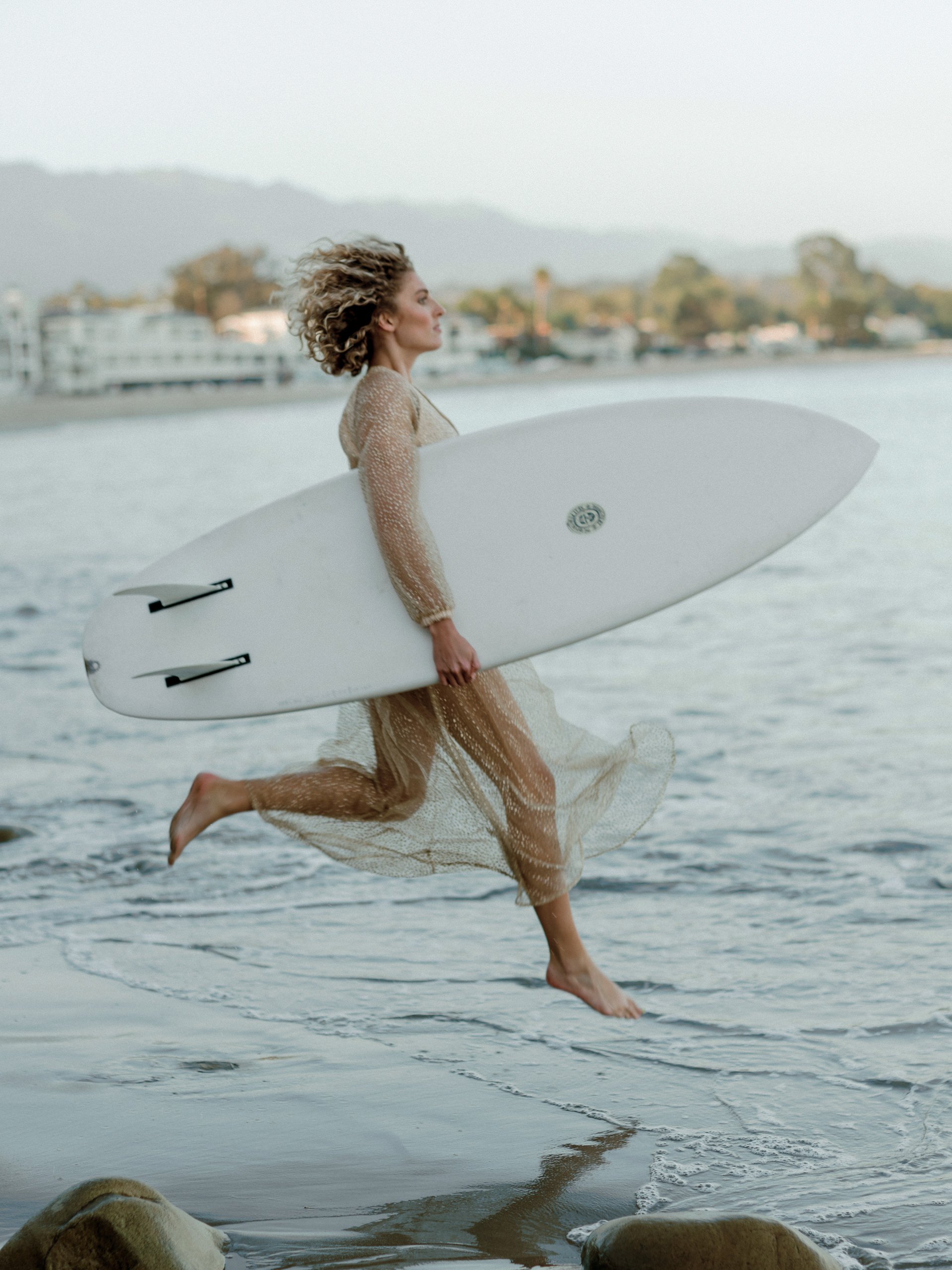 A woman running along the beach with a surfboard under her arm.