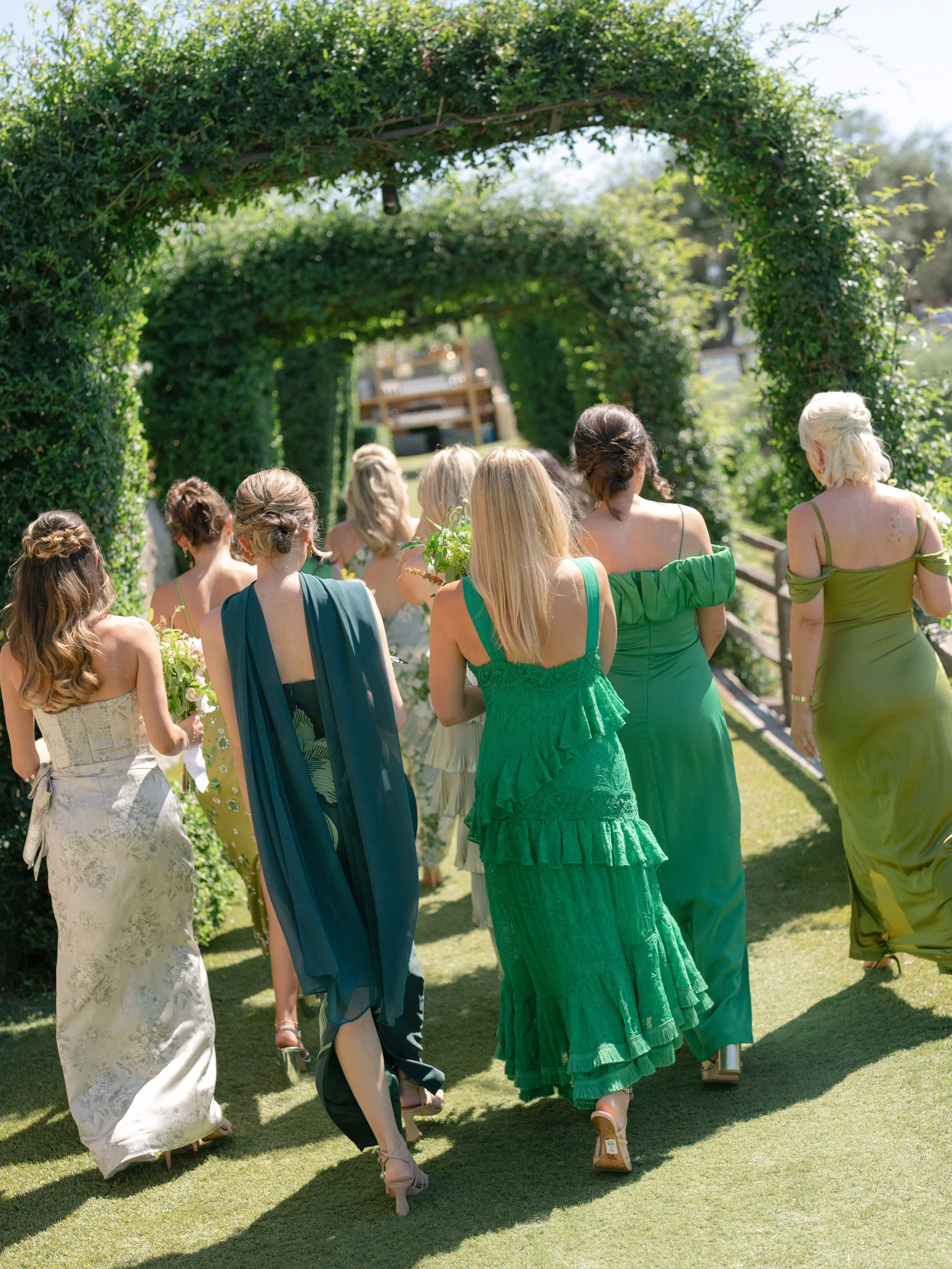 A group of women in colorful dresses walking under a green archway at an outdoor event.
