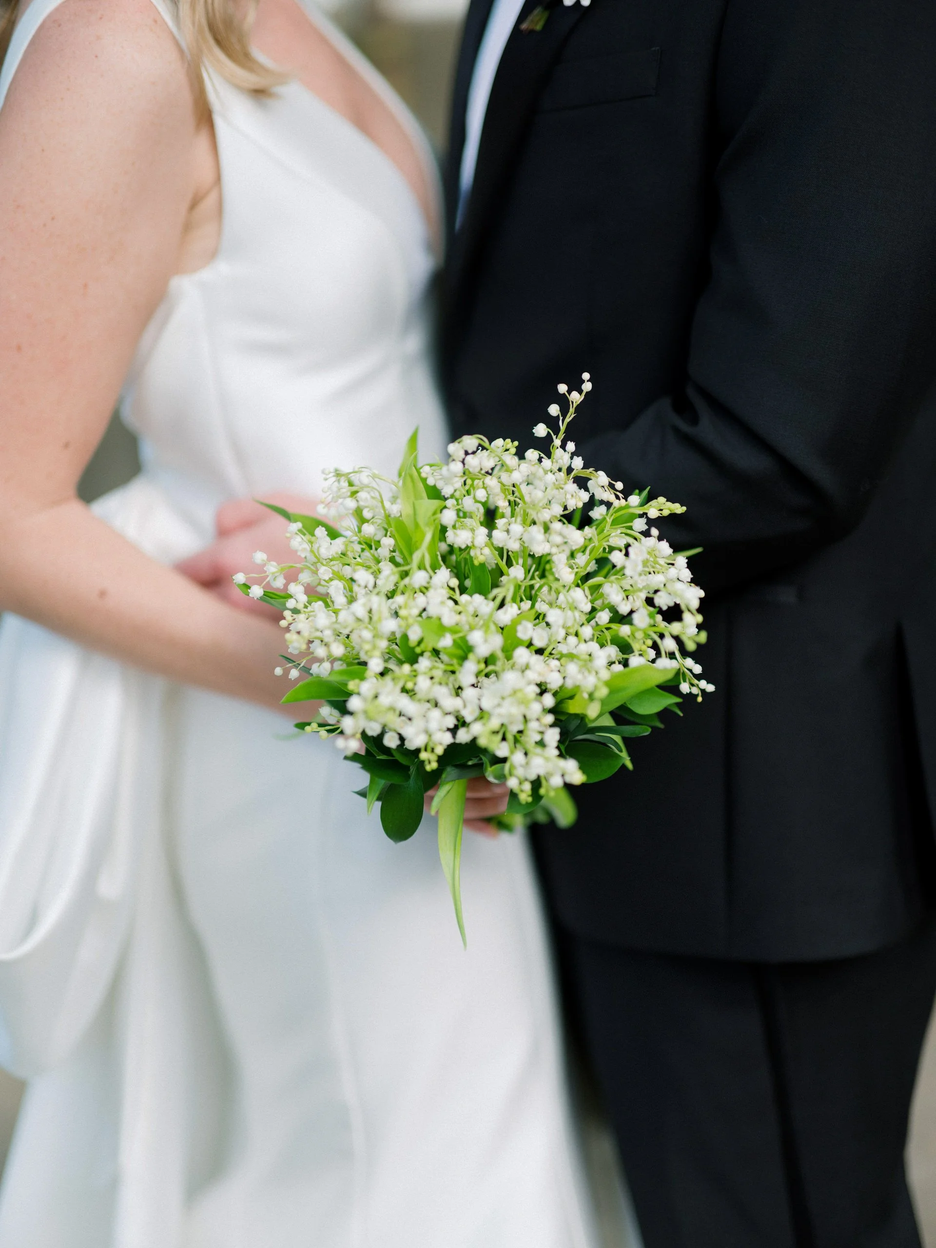 Close-up of a bride and groom holding a bouquet of white flowers during their wedding ceremony, with the bride wearing a white dress and the groom in a black suit.