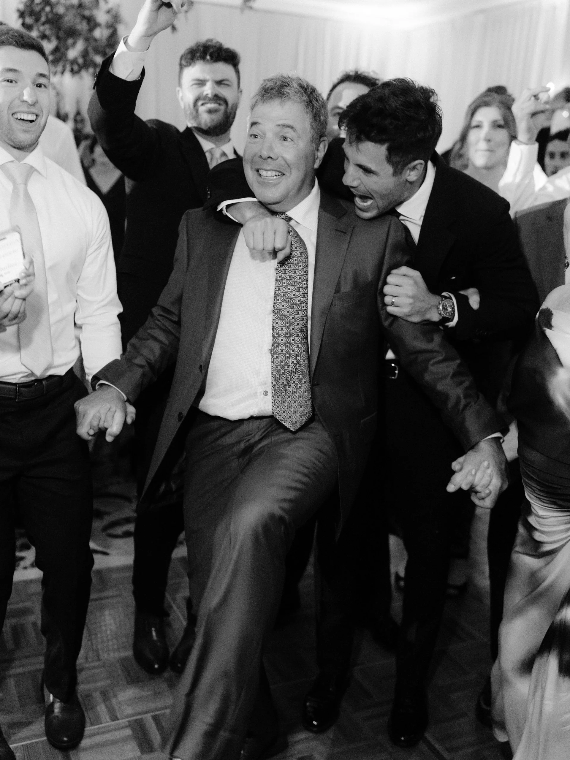 Group of men celebrating at a party, with some dancing and smiling cheerfully.