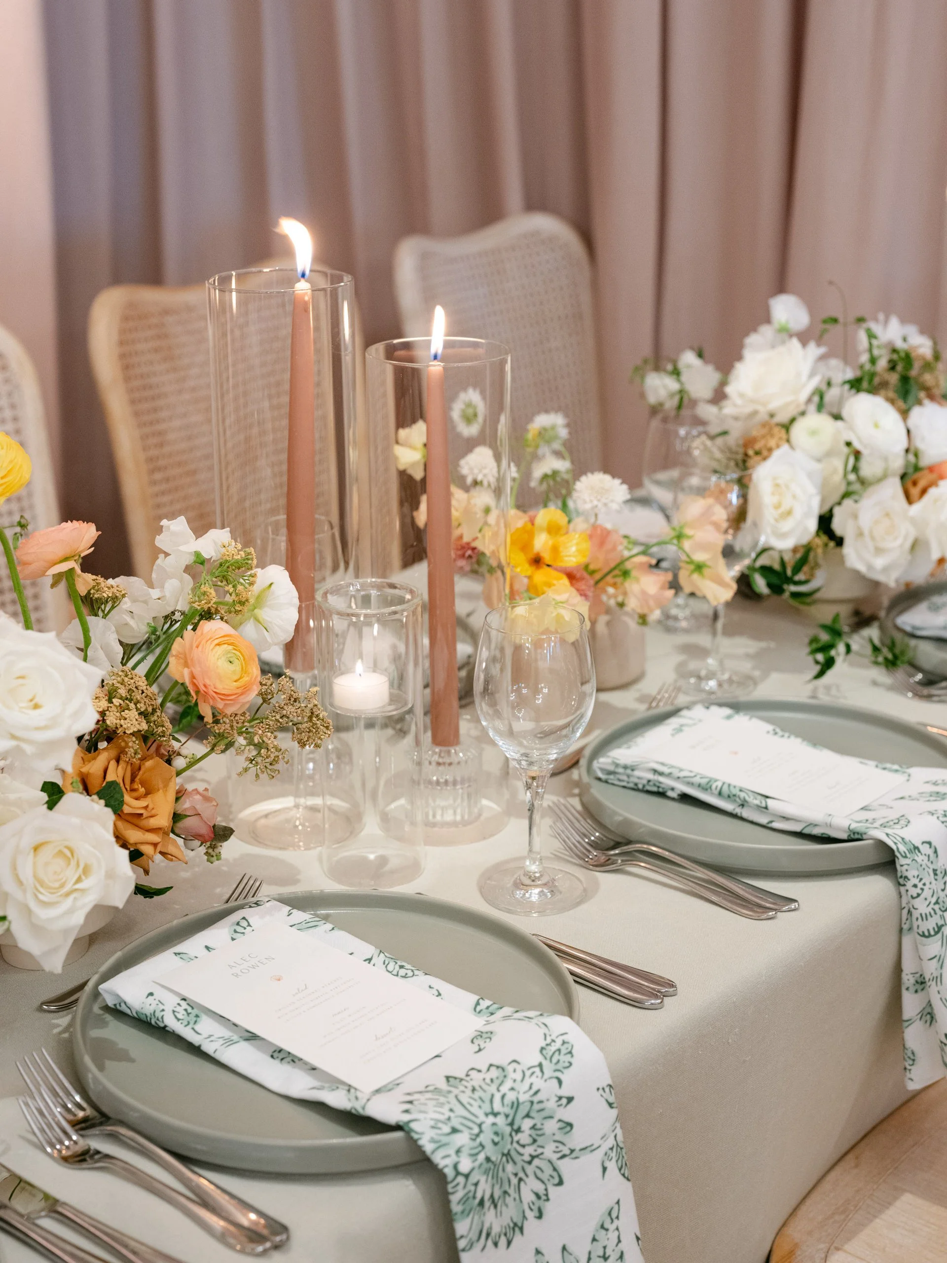Elegant table setting with floral centerpieces, tall candles, and place settings with plates, glasses, and silverware.