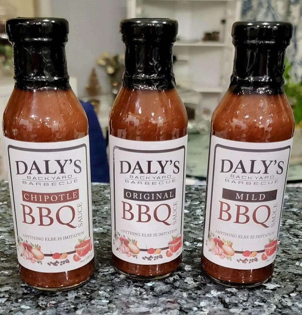 Three bottles of Daly's Backyard Barbecue sauce labeled Chipotle, Original, and Mild, placed on a granite countertop.