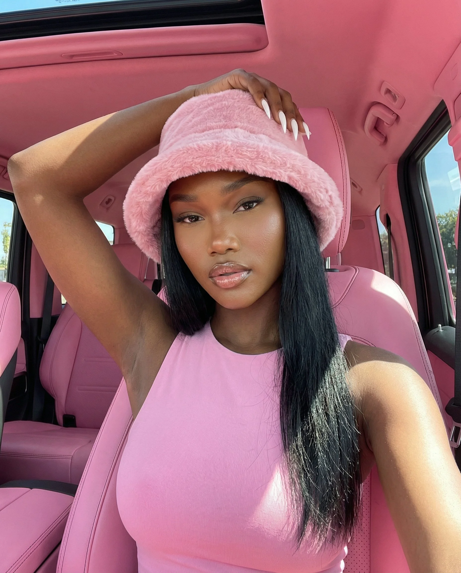 AI-generated realistic influencer avatar taking a selfie inside a pink car interior wearing a bucket hat, created using a copy-paste AI avatar prompt with natural lighting.  This signals:
