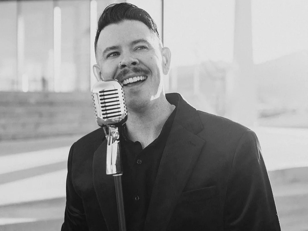 A man in a suit singing or speaking into a vintage microphone in a modern, well-lit indoor space.