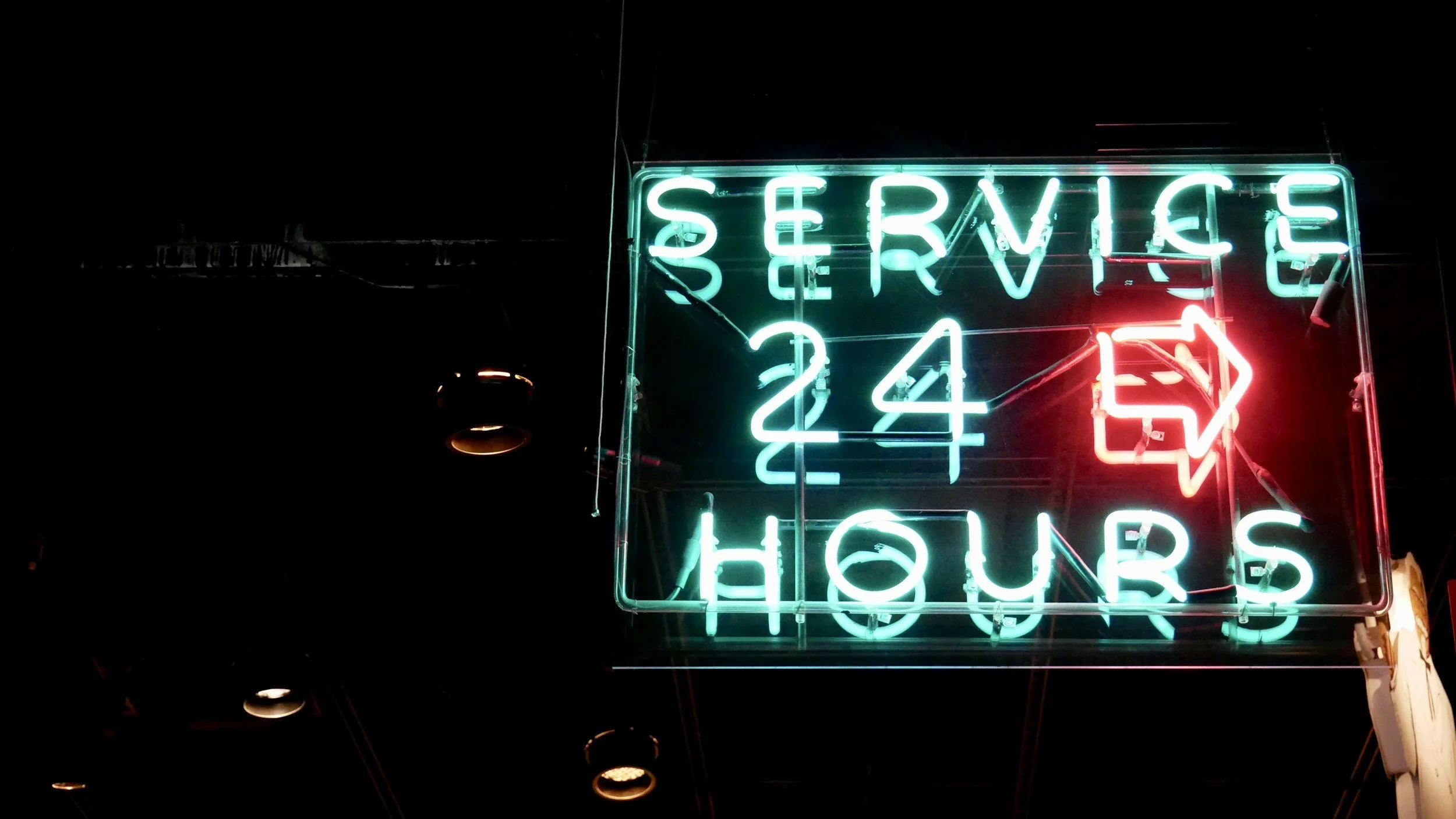 Neon sign advertising 24-hour service and hours for a business.