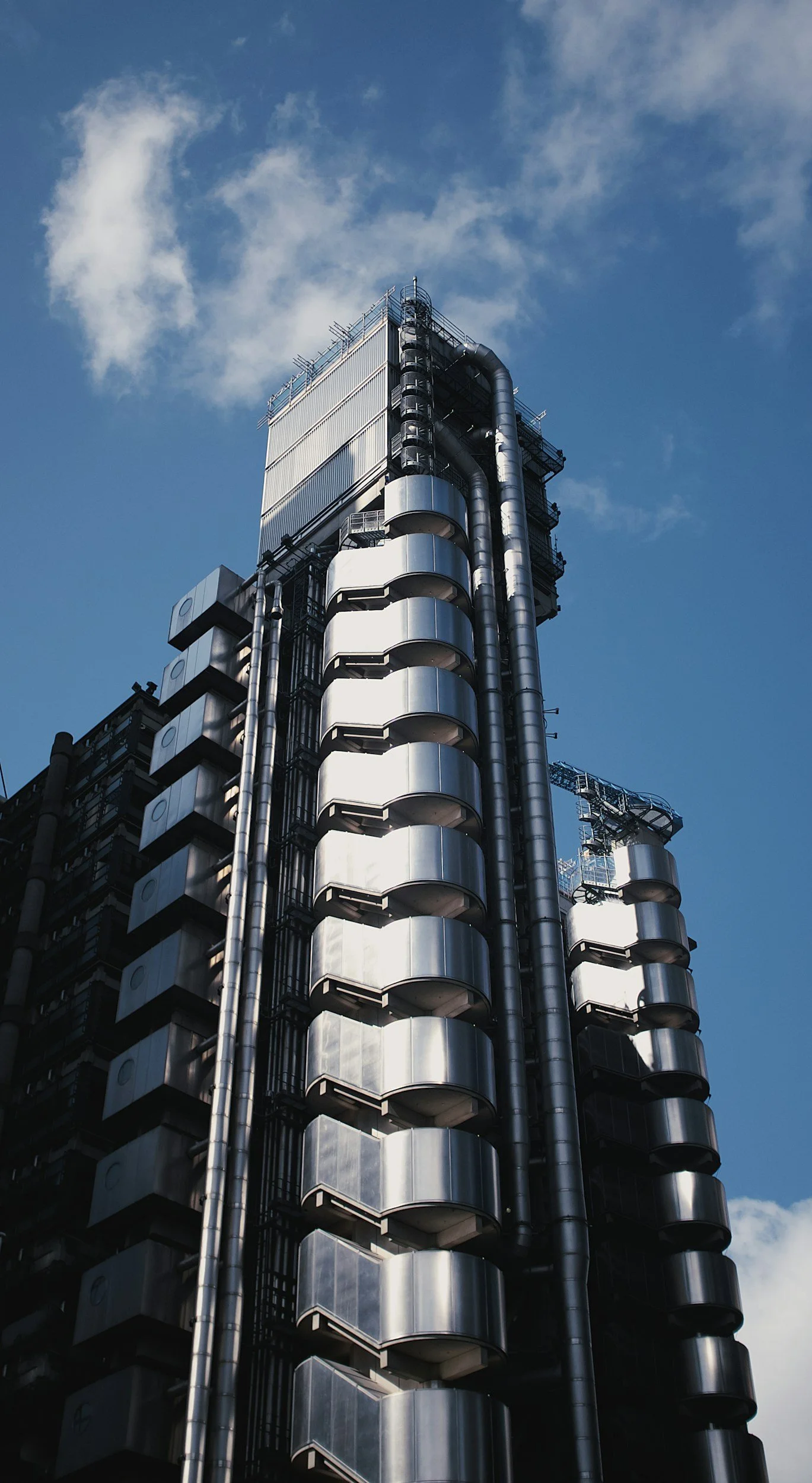 A tall modern skyscraper with shiny metallic exteriors and multiple curved balconies against a blue sky with some clouds.