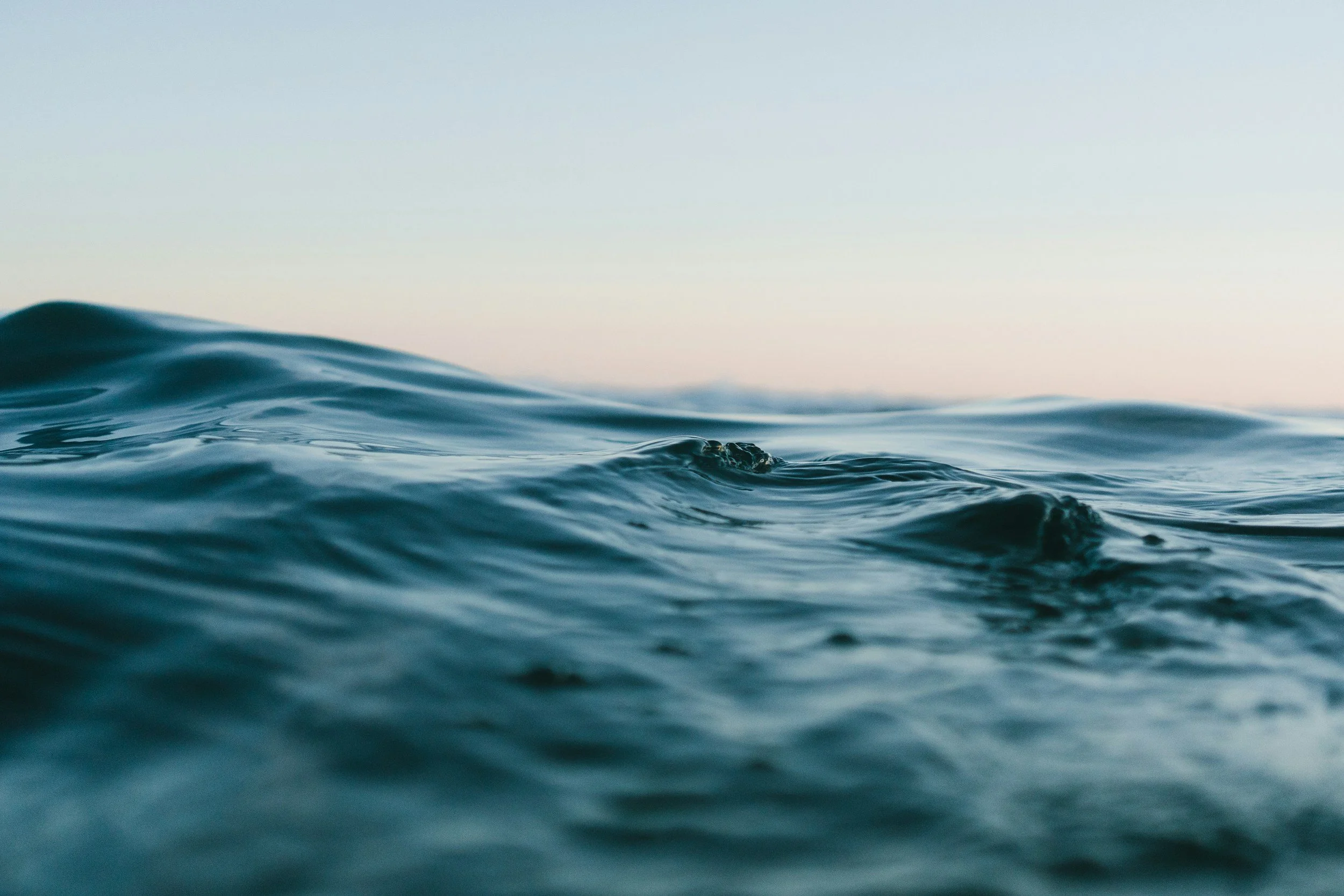 Close-up of ocean waves with a calm, pastel sky in the background.
