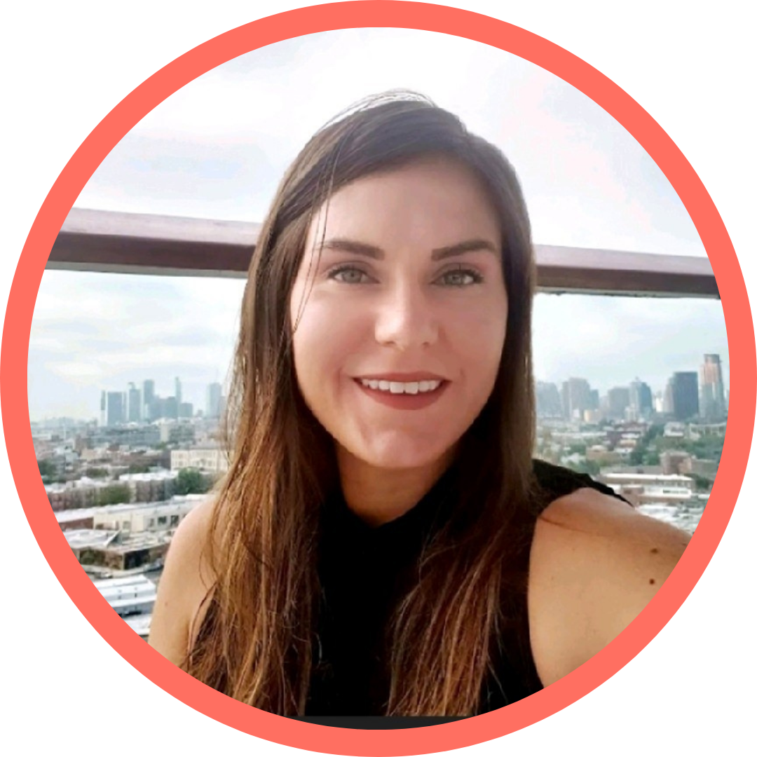 A young woman with long brown hair smiling outdoors with a city skyline in the background.
