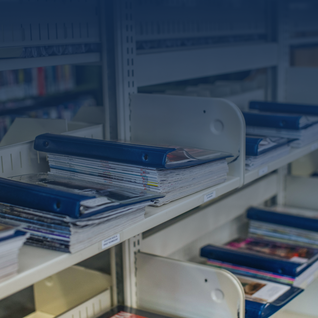 Shelf stocked with binders and documents in a library or office setting.