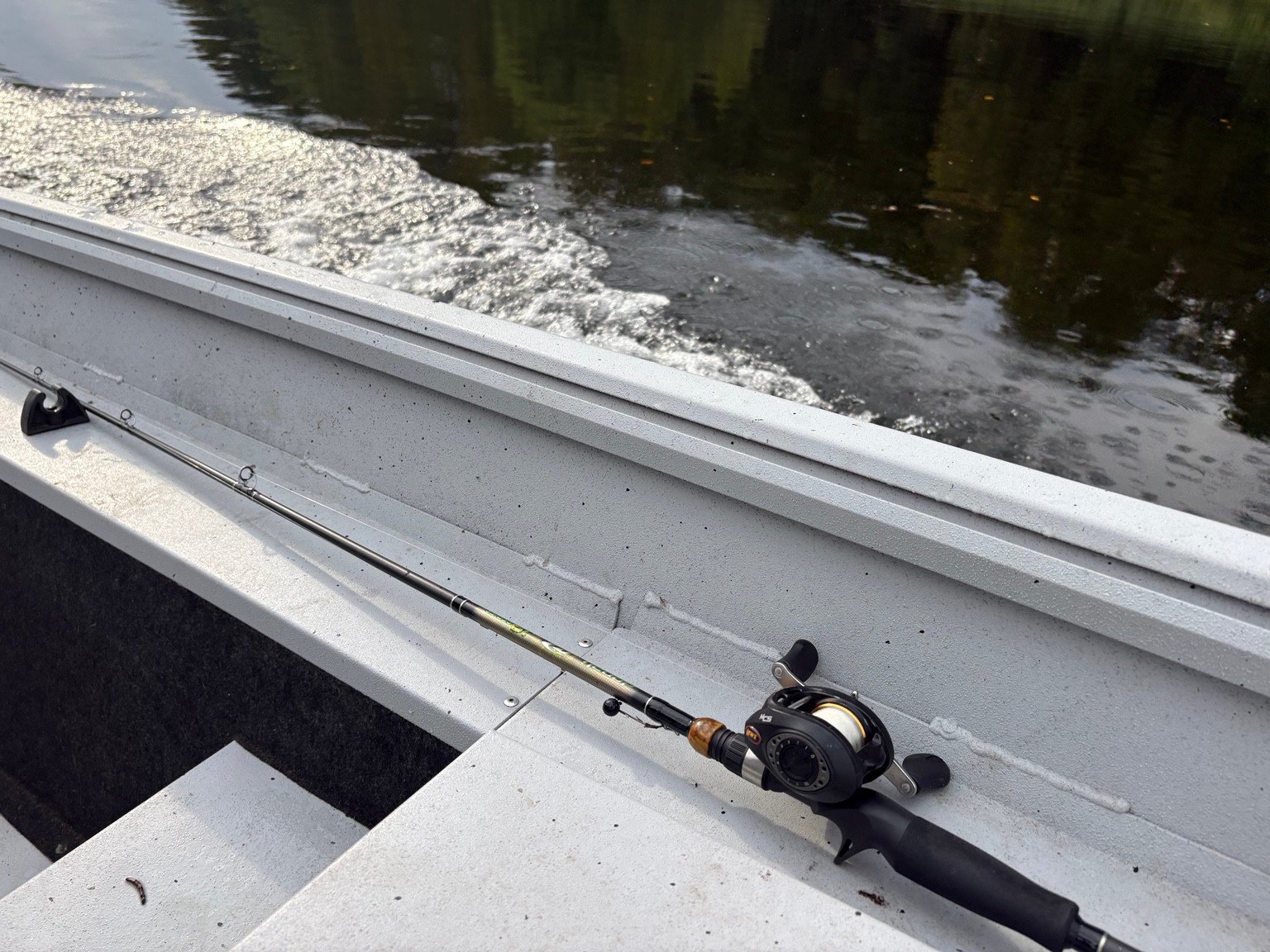 Baitcasting rod and reel resting along the side of an aluminum fishing boat.
