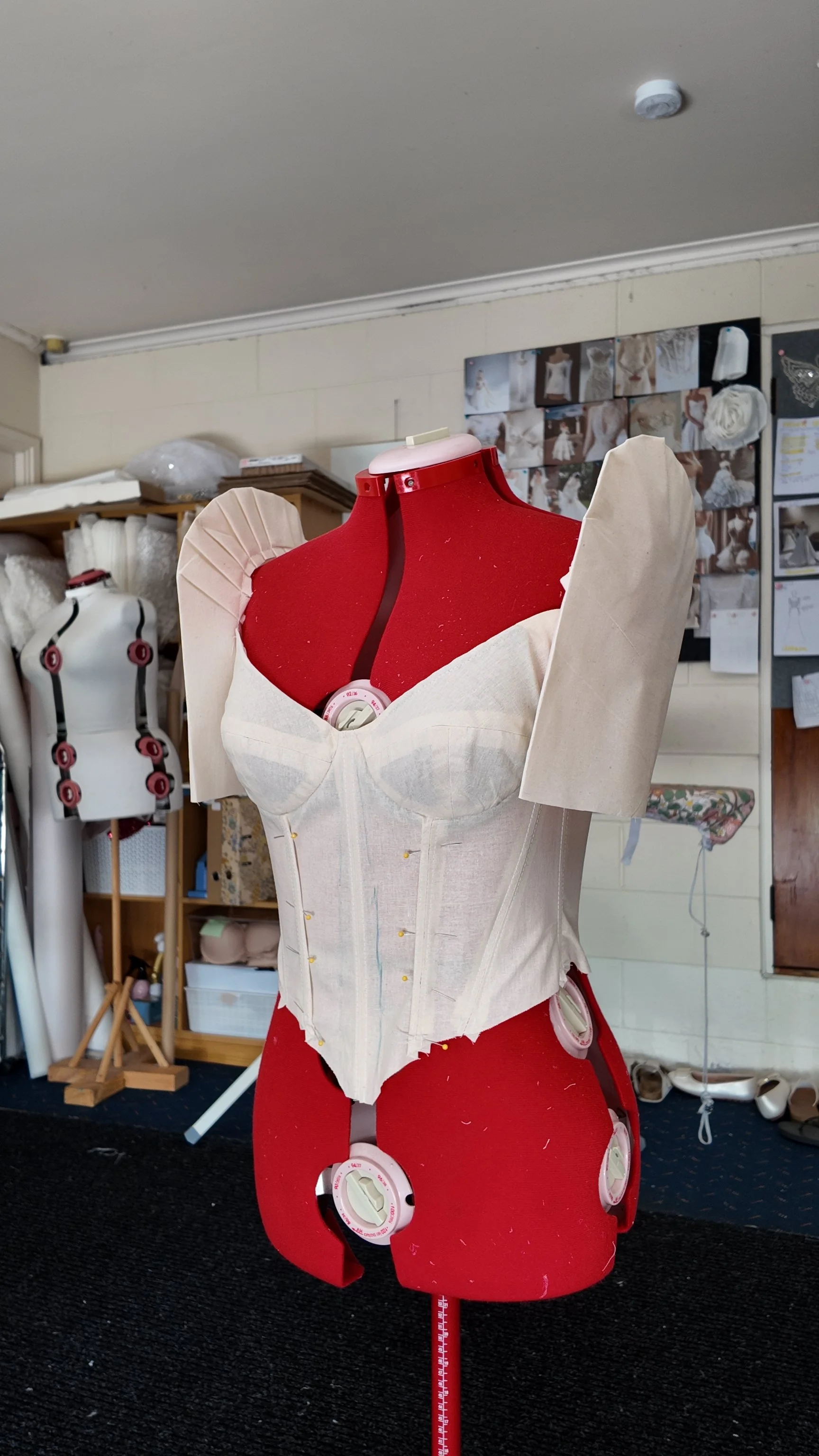 A dress form wearing a partially constructed corset and shoulder pads in a sewing studio.