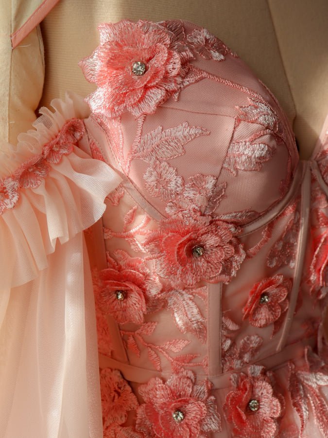 Close-up of a pink, floral embroidered dress with rhinestone accents and ruffled fabric detail.