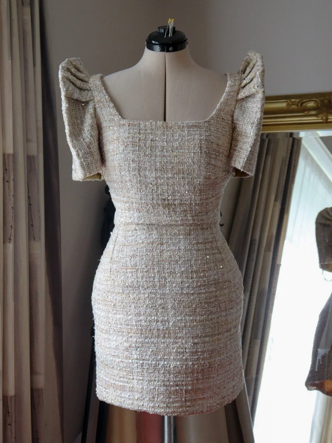 A beige, textured, fitted dress with puffed short sleeves, displayed on a mannequin.