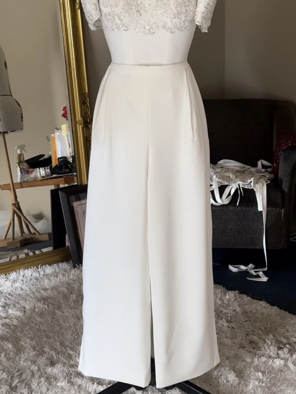 White wedding dress with lace bodice and wide-leg pants on a mannequin in a room.