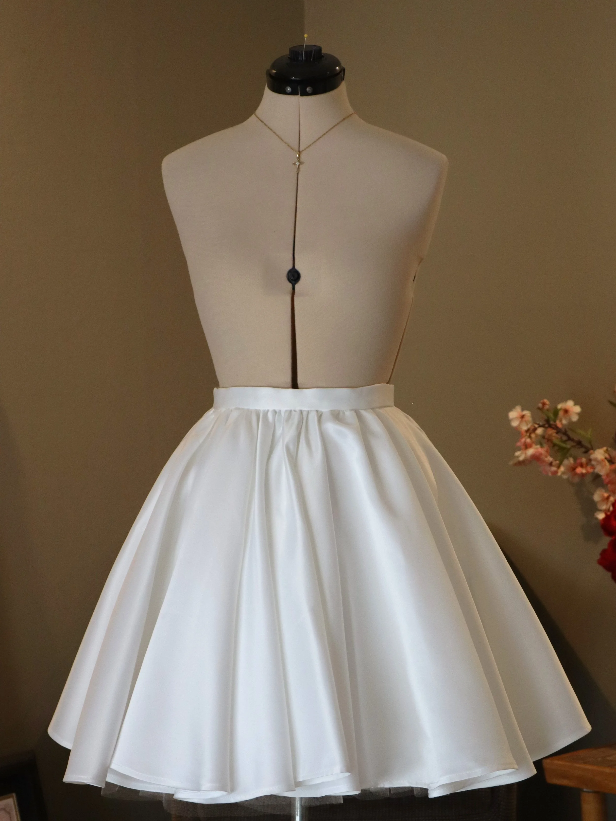 A mannequin torso wearing a wedding dress with a satin full skirt and a simple necklace