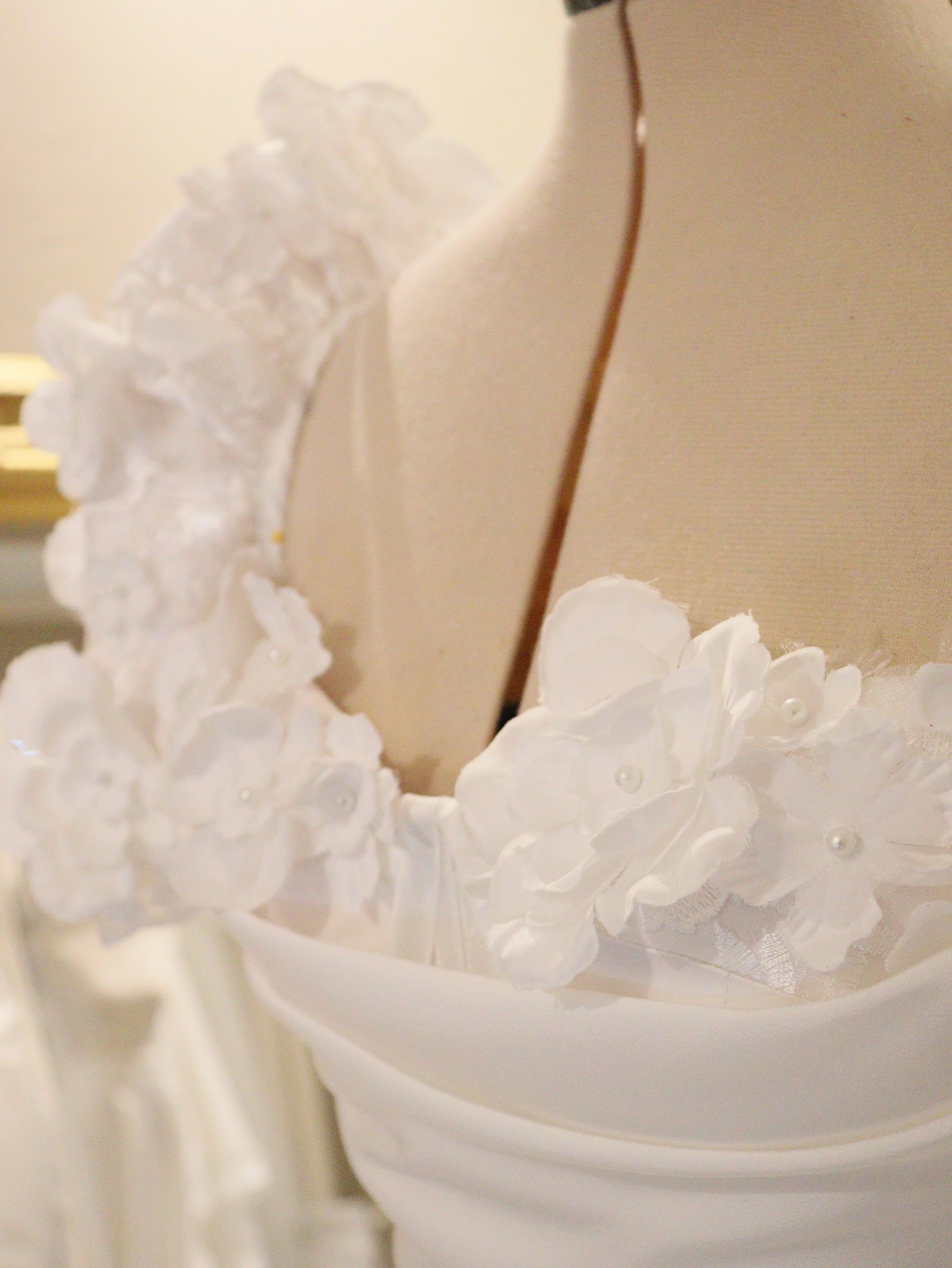 Close-up of a white wedding dress with floral embellishments and pearl accents near the neckline.