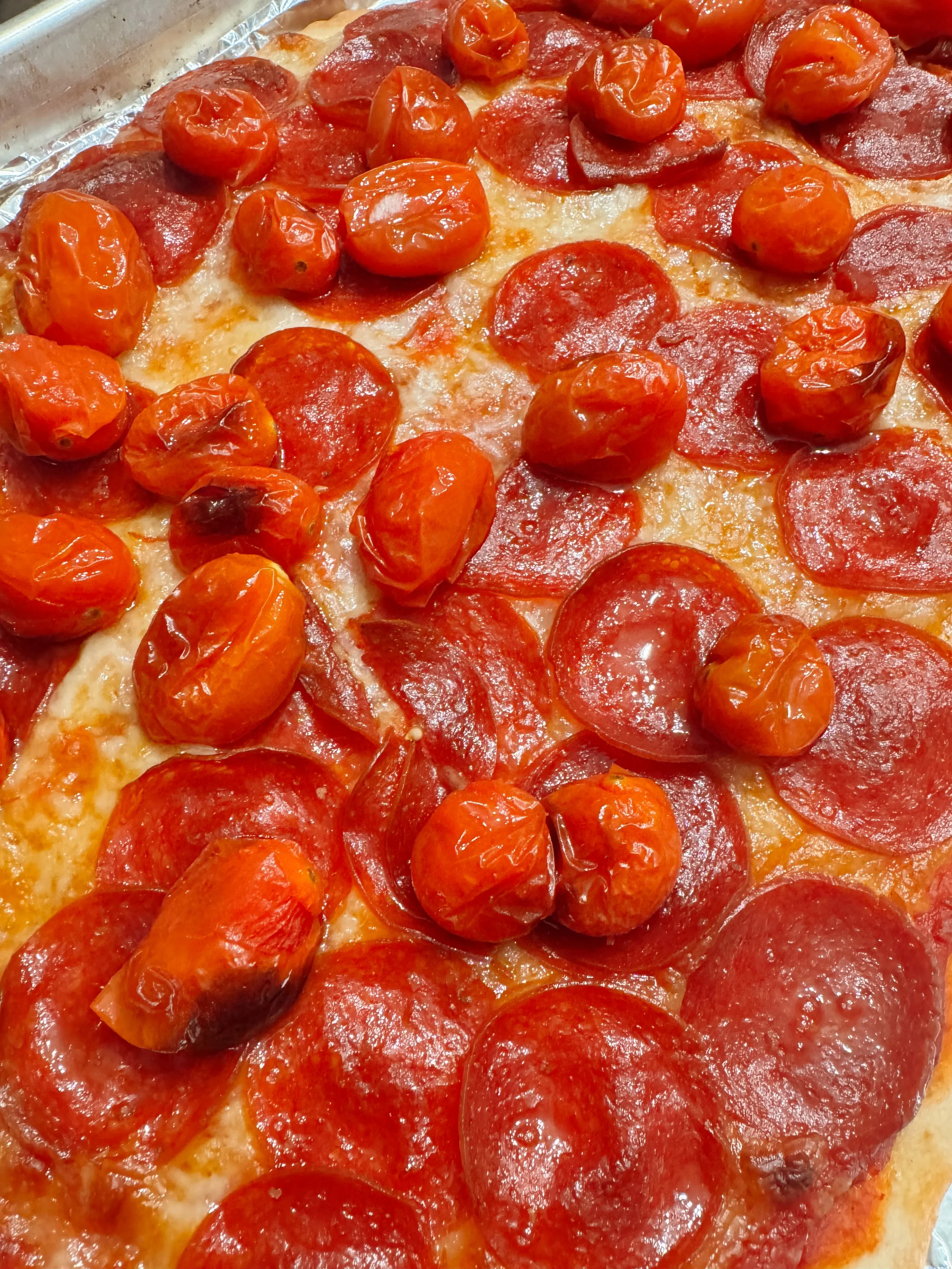 A close-up of a pepperoni and cherry tomato pizza.