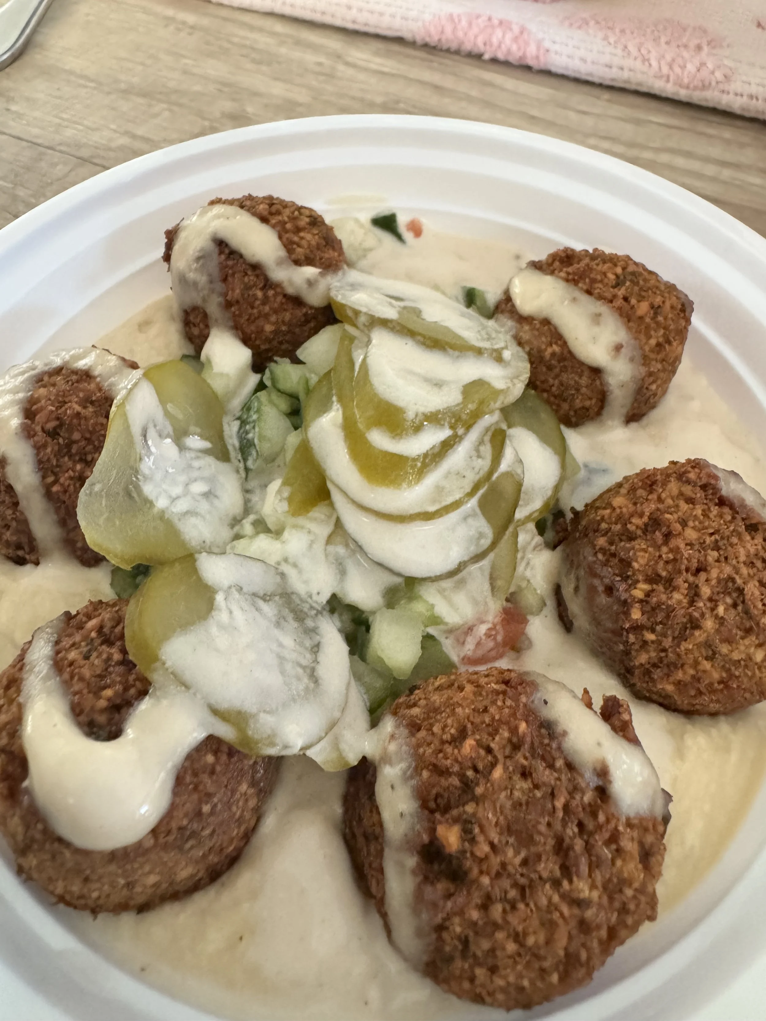 Fried food balls with creamy sauce, pickles, and chopped vegetables in a white bowl.