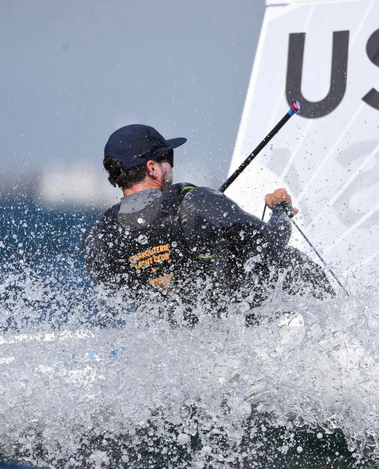 A person sailing a boat on the water, wearing a helmet and a jacket, with a spray of water around them.