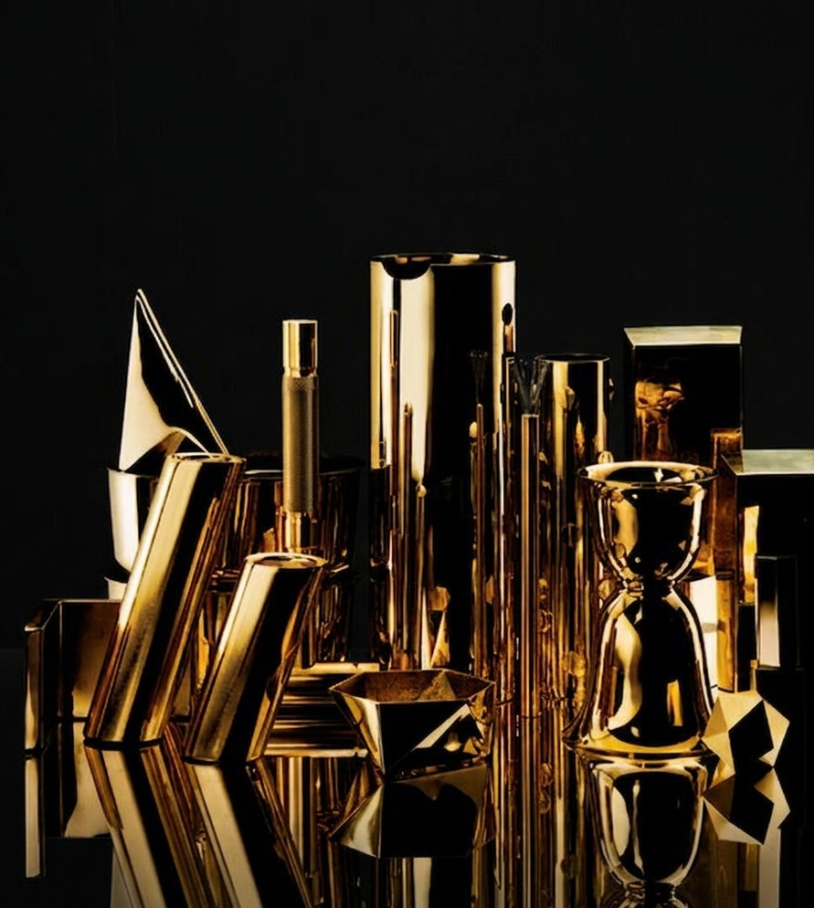 Collection of shiny gold and black decorative objects, including vases, cups, and geometric shapes, arranged on a reflective surface