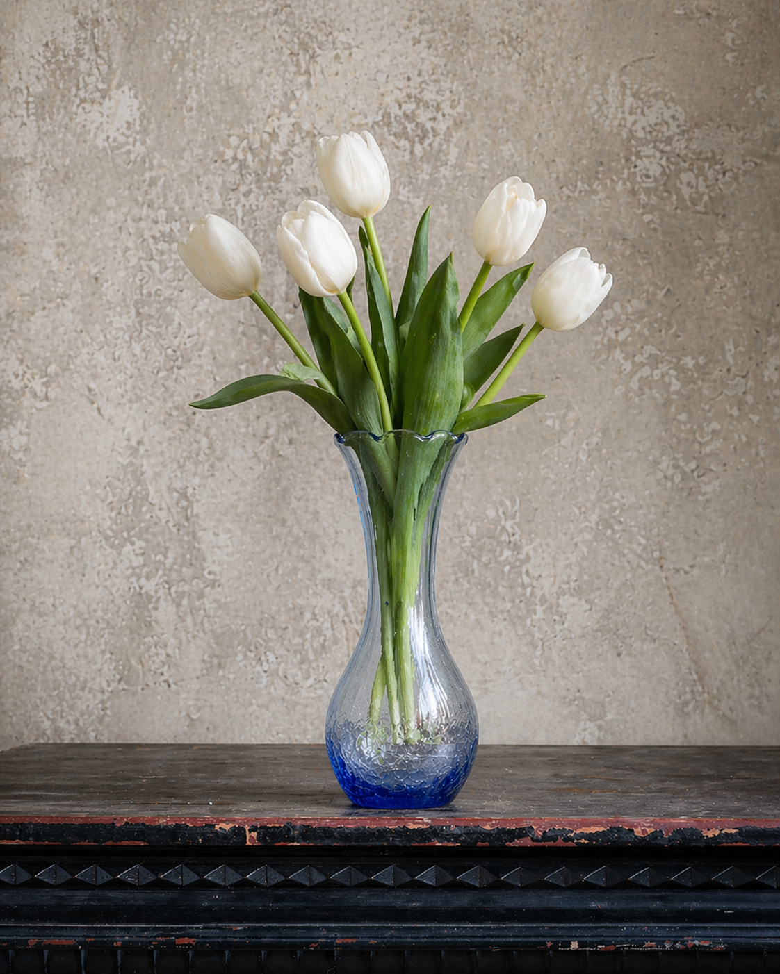A bouquet of white tulips in a blue-tinted glass vase.