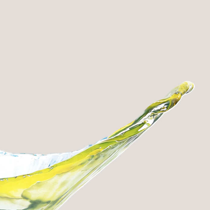 Close-up of a splash of yellow and green paint on a reflective surface with a plain white background.