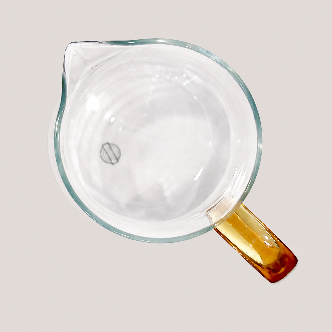 Top view of a clear glass measuring cup with a yellow handle, empty, on a plain light background.