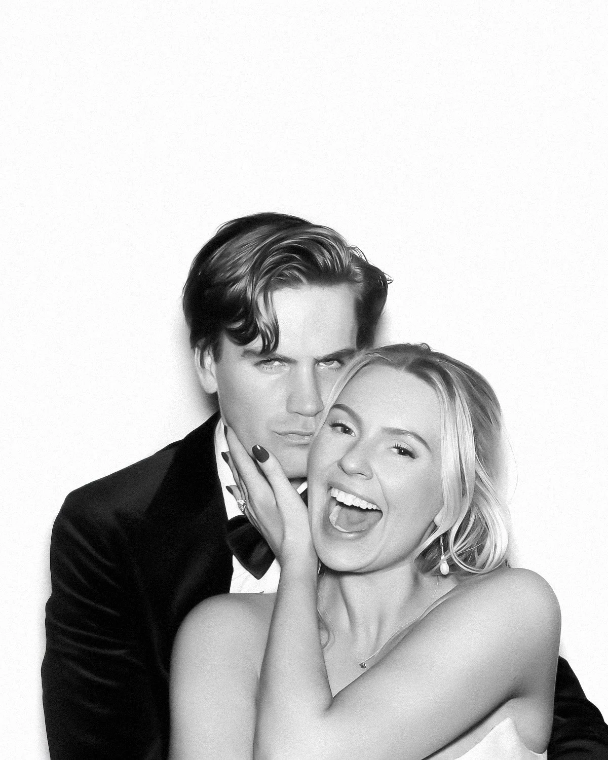 Black and white portrait of a man and woman, with the woman smiling and winking, and the man looking serious, against a plain white background.