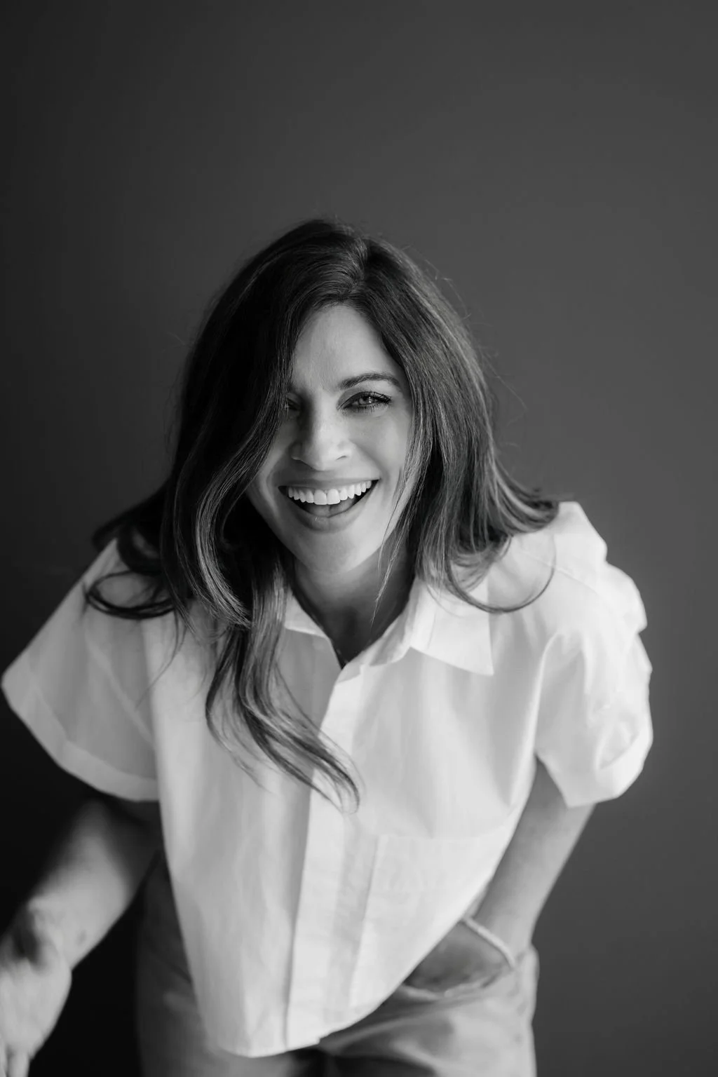 Black and white portrait of a woman smiling, wearing a white shirt with her hair styled in loose waves.