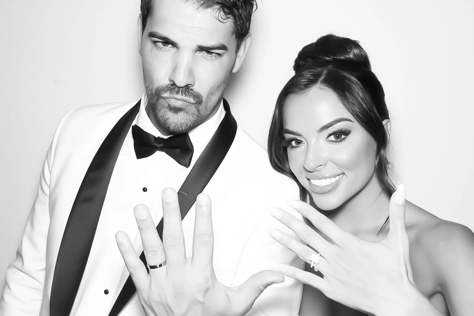 Black and white photo of a man and woman dressed formally, showing off rings on their hands in a model pose.
