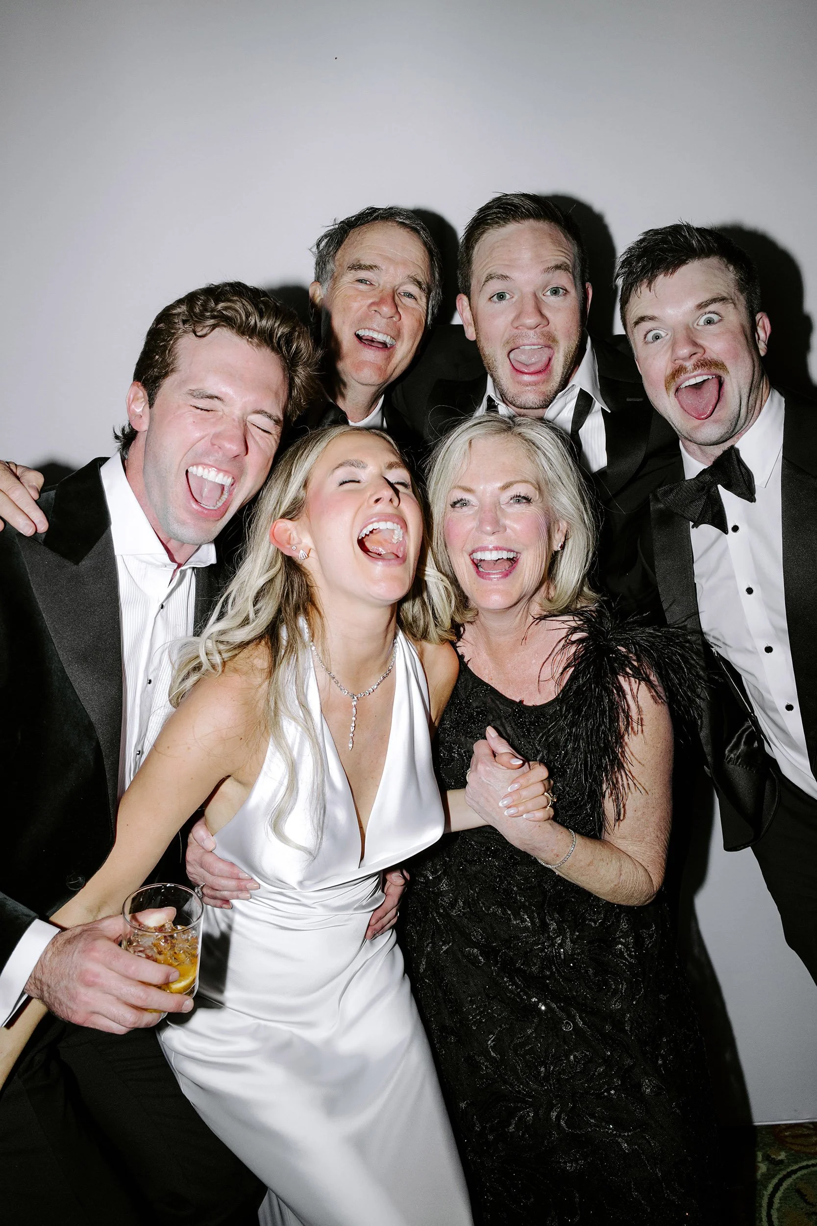 Group of seven people dressed in formal attire, smiling and laughing at a celebration.