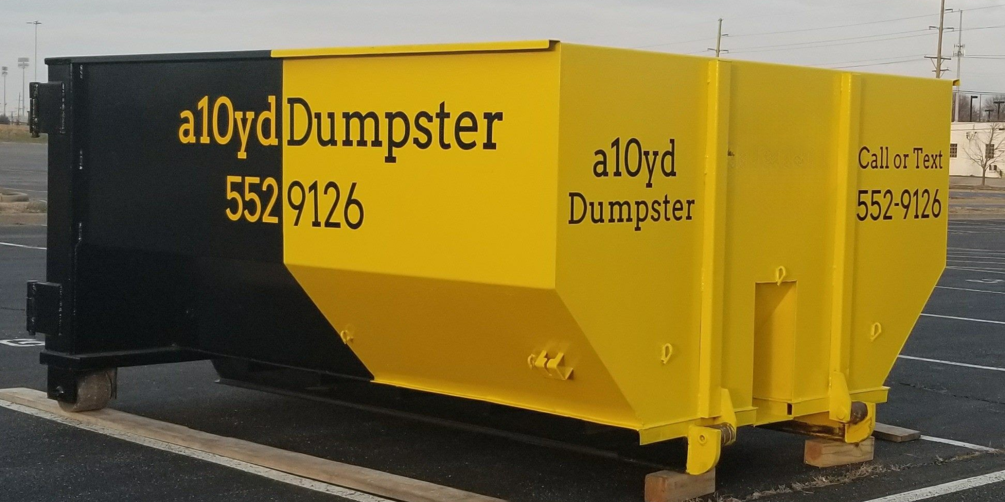A yellow and black dumpster in a parking lot with the text 'aloyd Dumpster' and a phone number 552‑9126 on the side.
