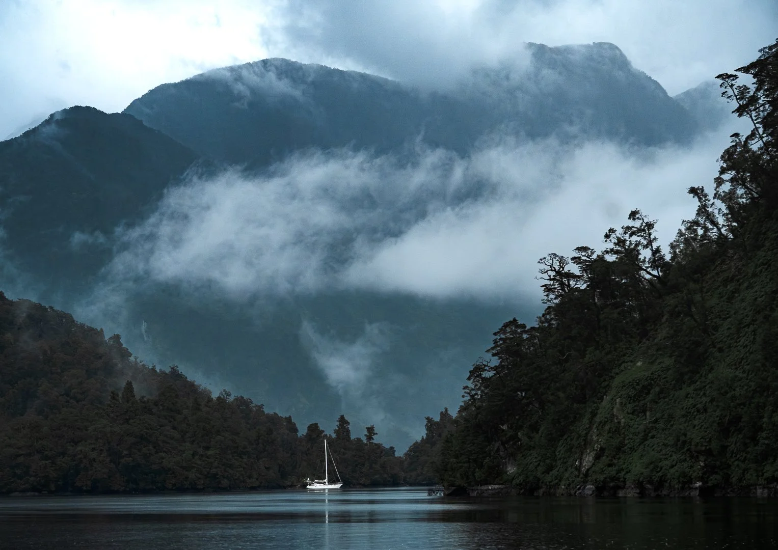 Sailboat on misty lake with mountains behind