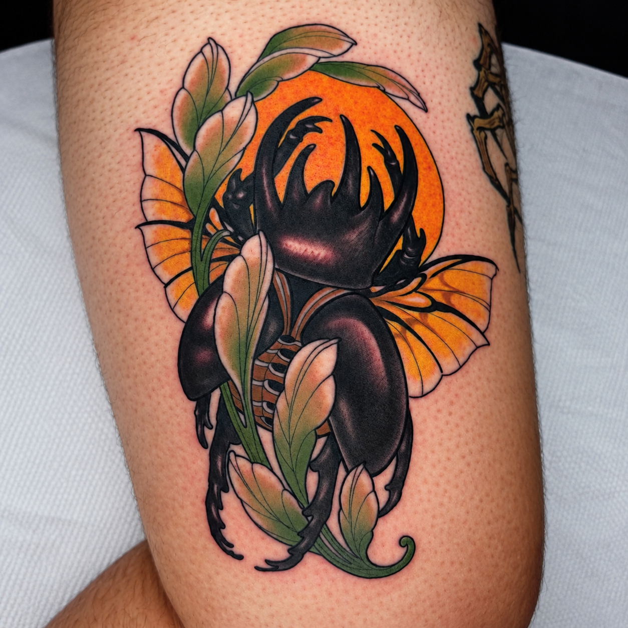 Orange and black beetle tattoo with botanical details by Adrian Aguirre.