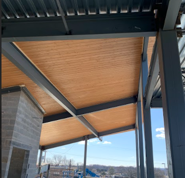 Under construction steel framework with a wooden ceiling, overlooking a landscape with blue sky and clouds.
