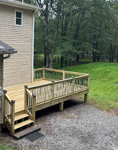 Wooden deck outside a house with stairs, surrounded by grass and trees.