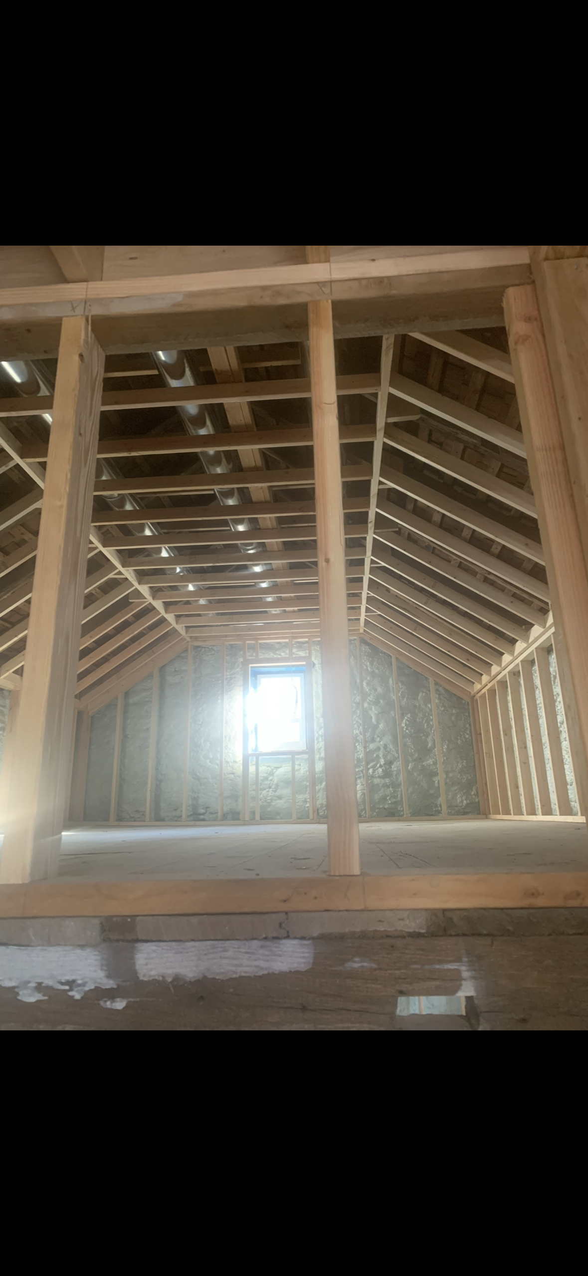 Interior view of a room under construction with exposed wooden framing and a small window at the end.