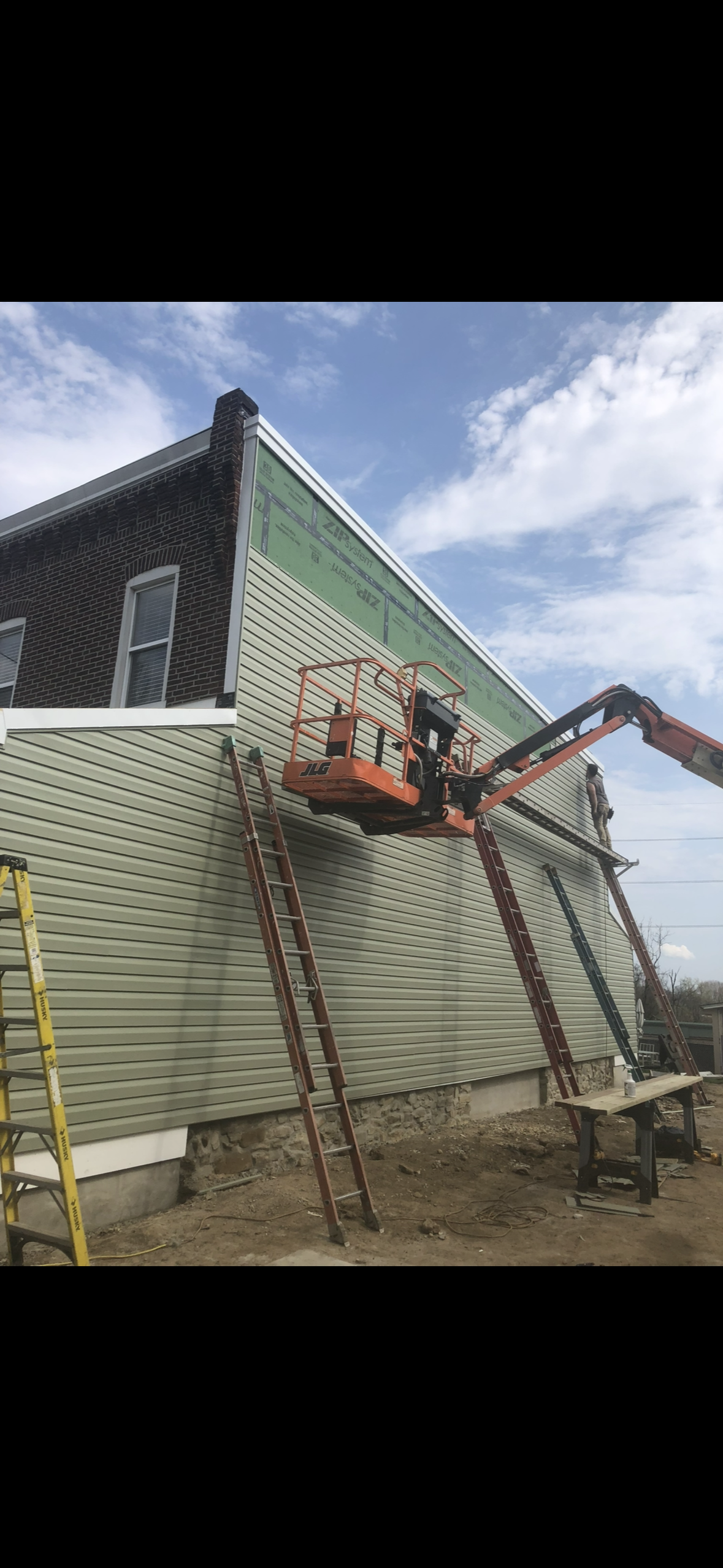 Construction workers installing siding on a building with a cherry picker lift.
