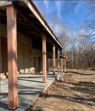 Back porch of a house with wooden support beams and a concrete patio, surrounded by trees with no leaves.